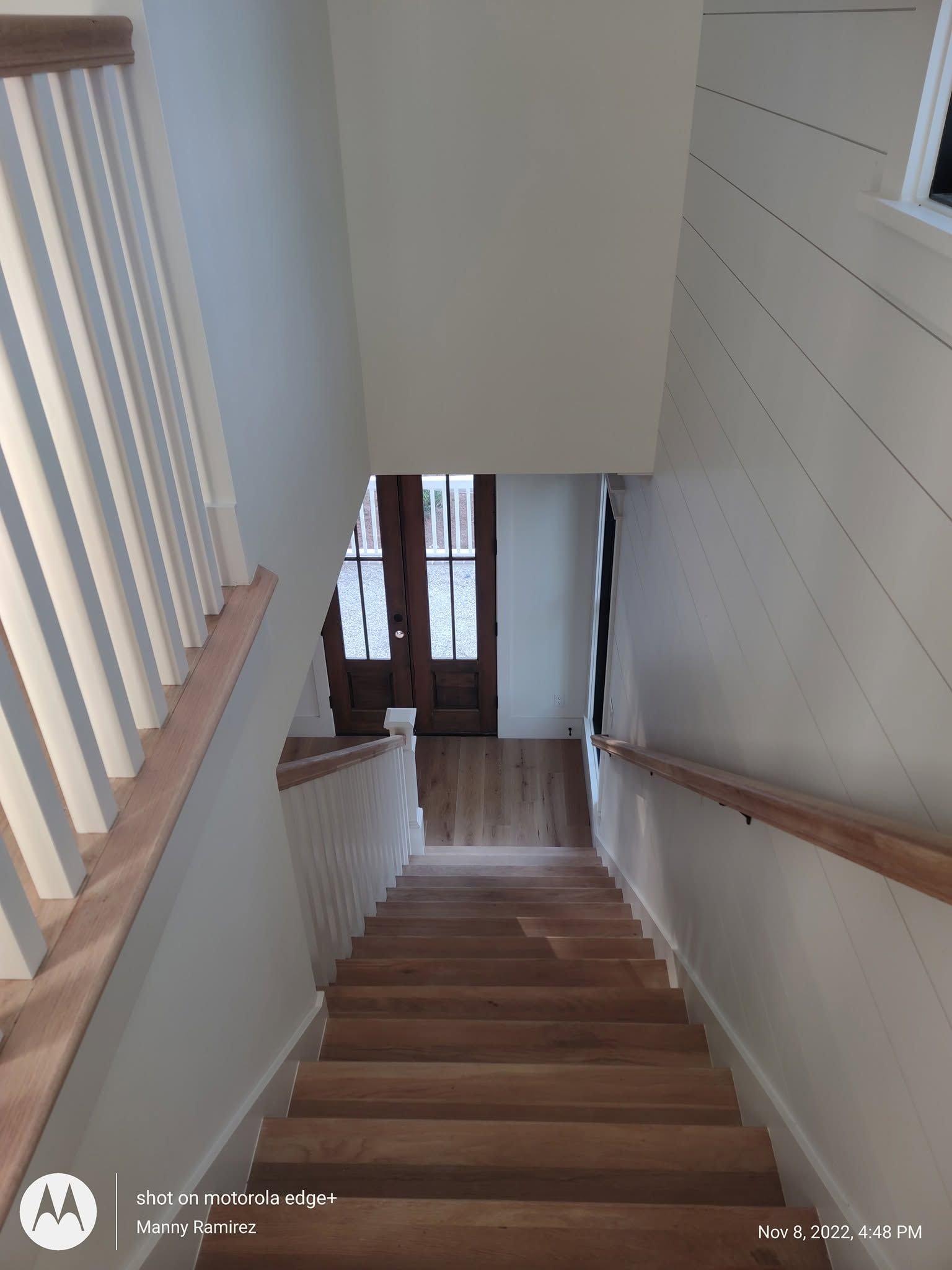 White-painted staircase looking down to a stained entry door and shiplap wall