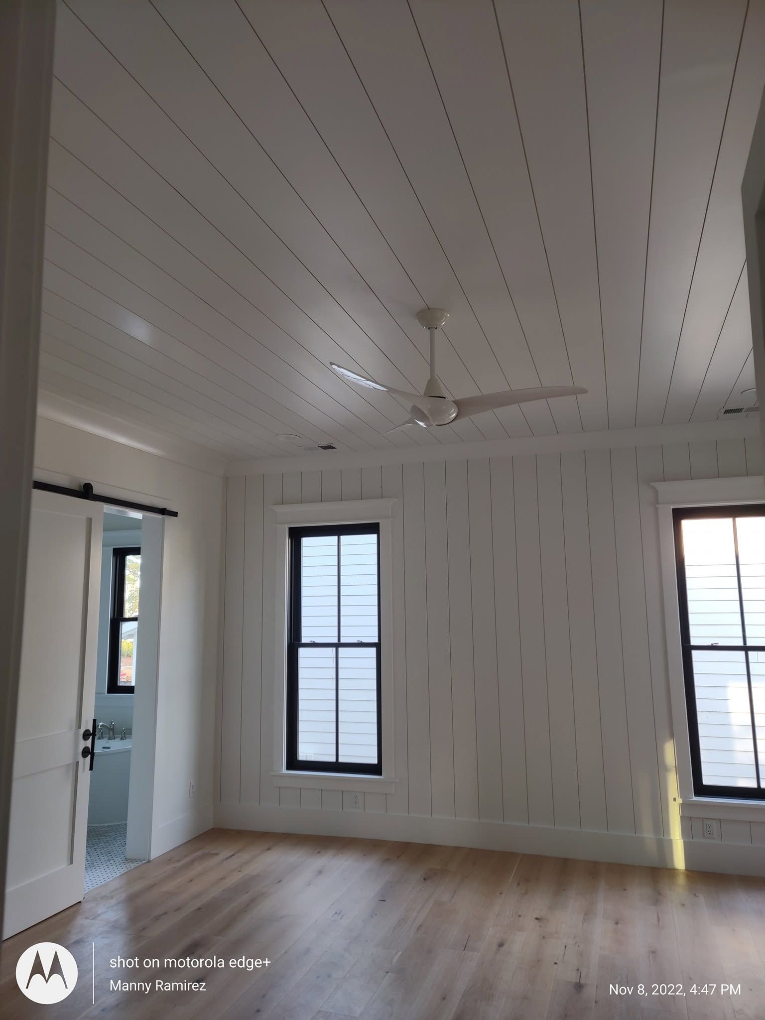White shiplap bedroom with black-trimmed windows and ceiling fan